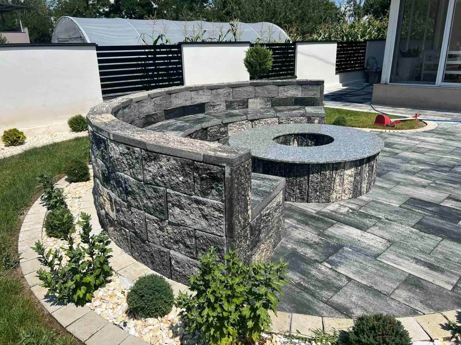 Concrete edging enclosing a gravel bed with shrubs, beside lawn and paving.
