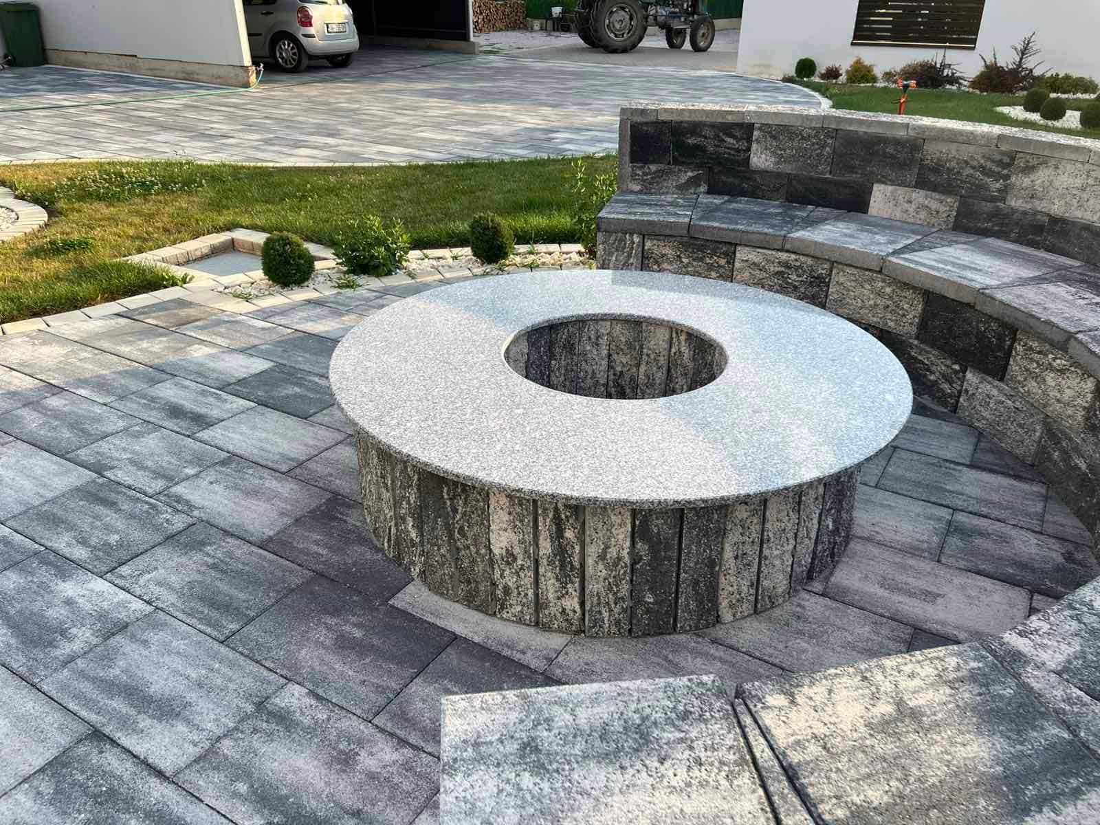 Circular concrete element with a seating step, surrounded by curved walls and paving.