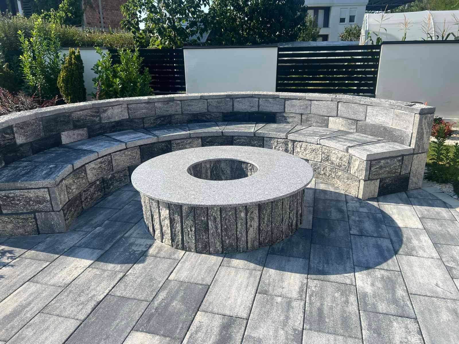 Curved wall with a concrete coping forming a seat around a paved area.