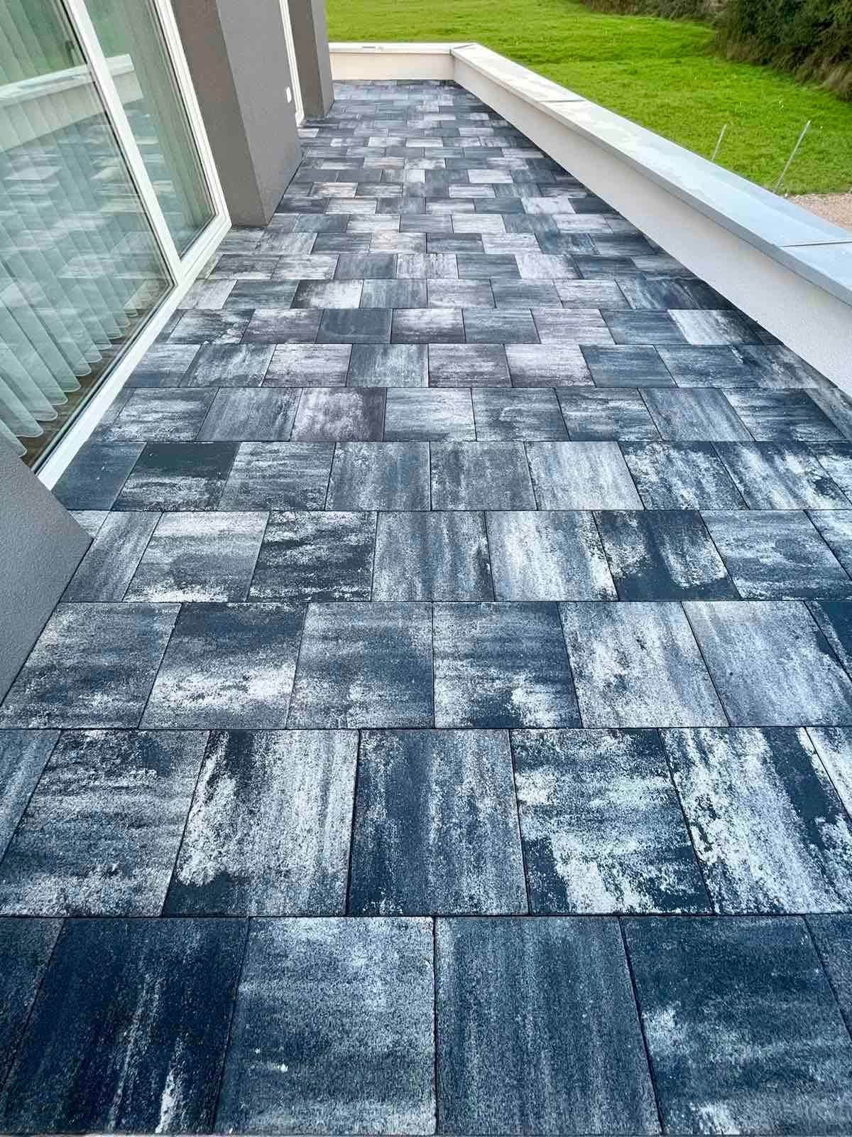 Paved strip along the glazed side of the house, lawn beyond.