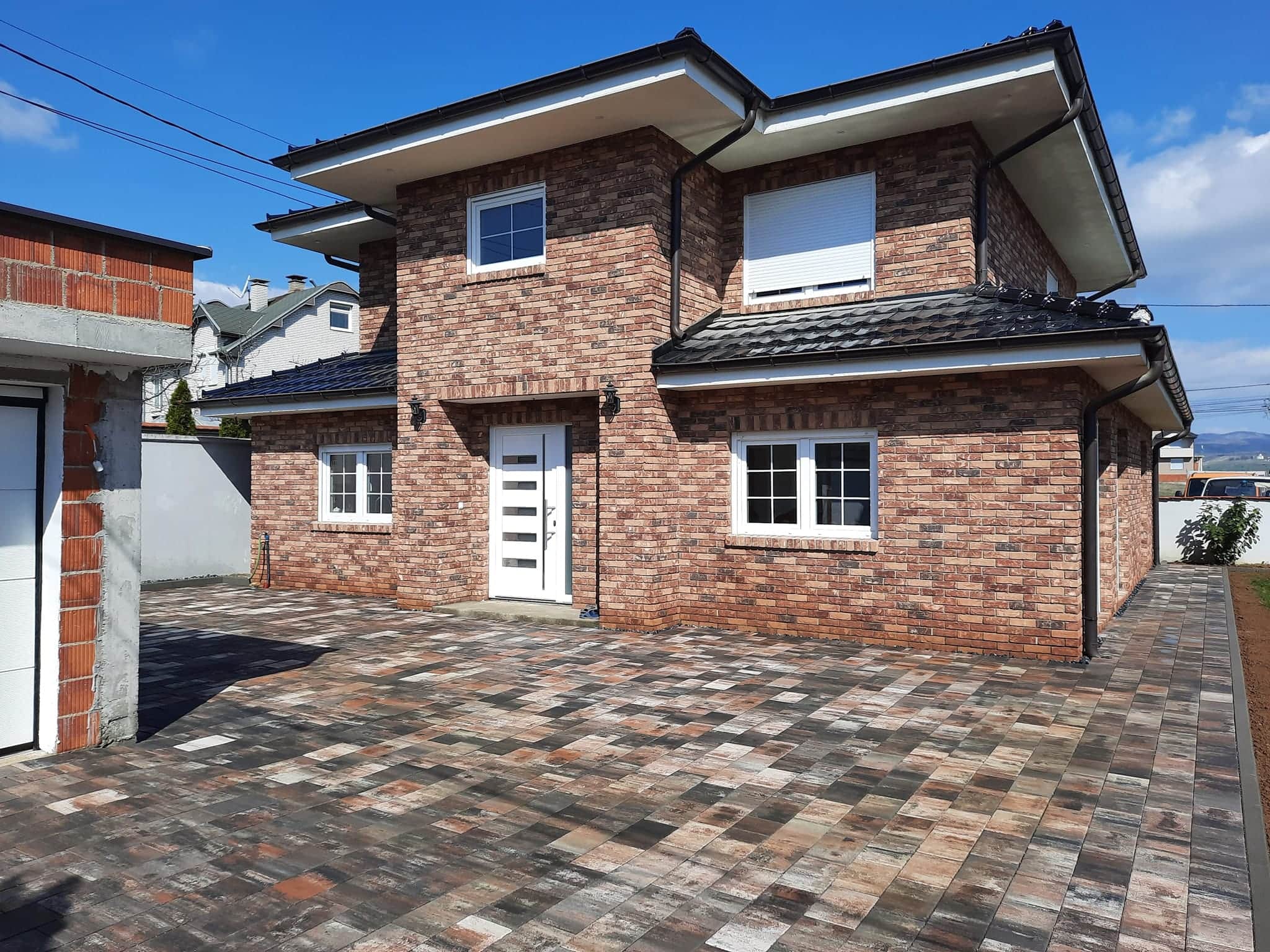 Two-storey brick house with a wide paved forecourt in mixed warm tones.