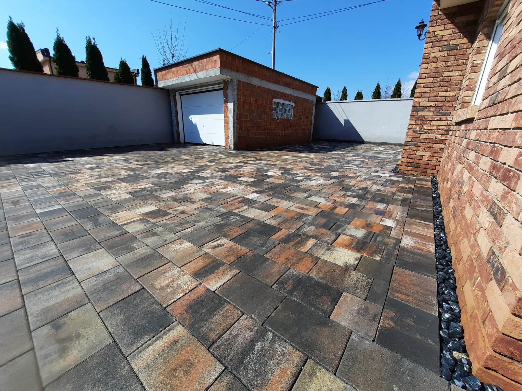 Paved forecourt running to a white boundary wall and a brick outbuilding.