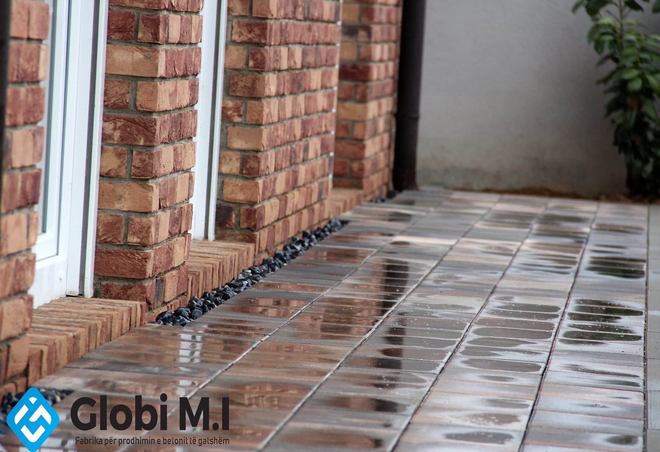Wet paving in a narrow passage between a brick pier and a rendered wall.