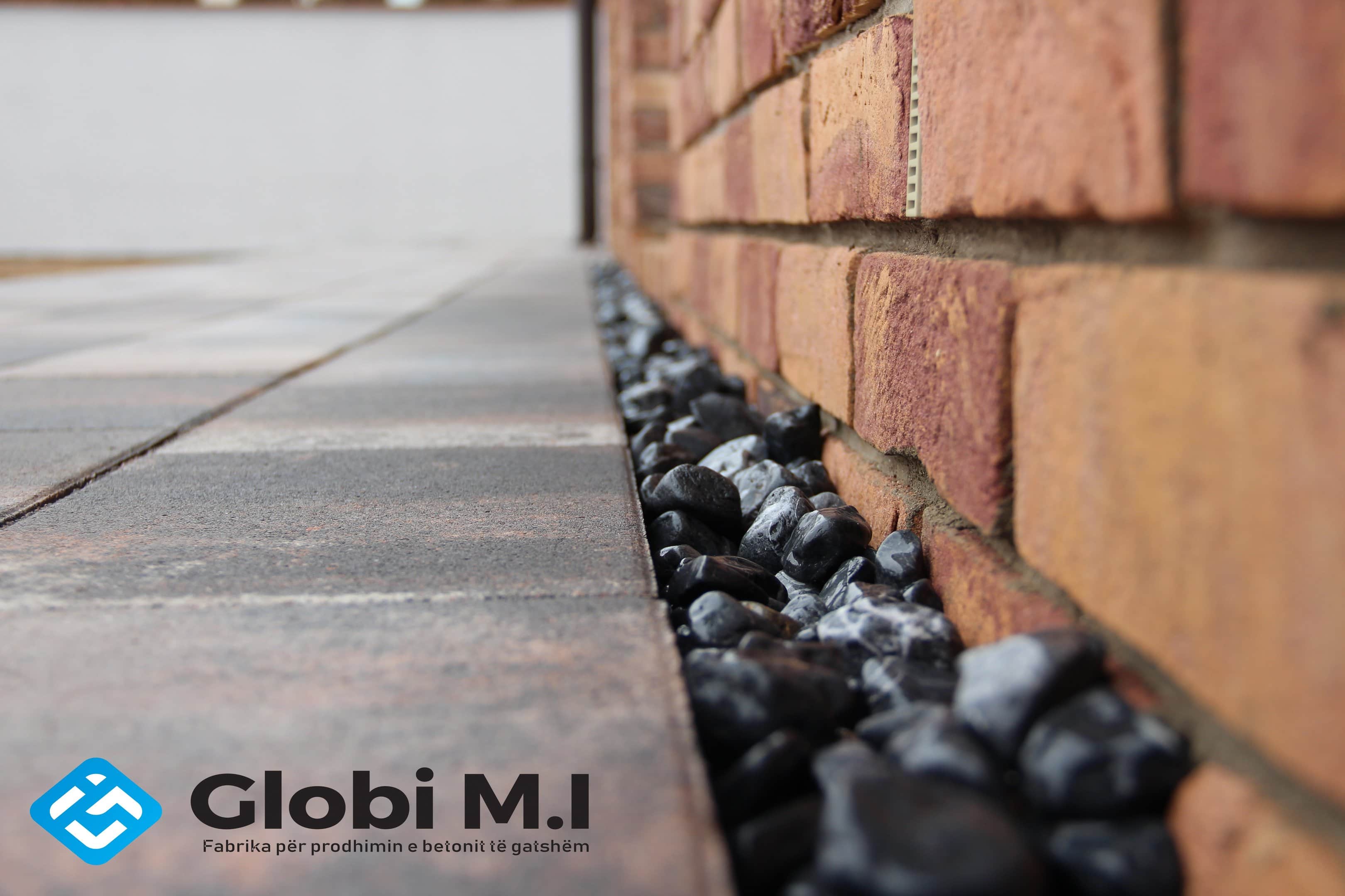 Strip of black pebbles between the paved surface and the brick wall.