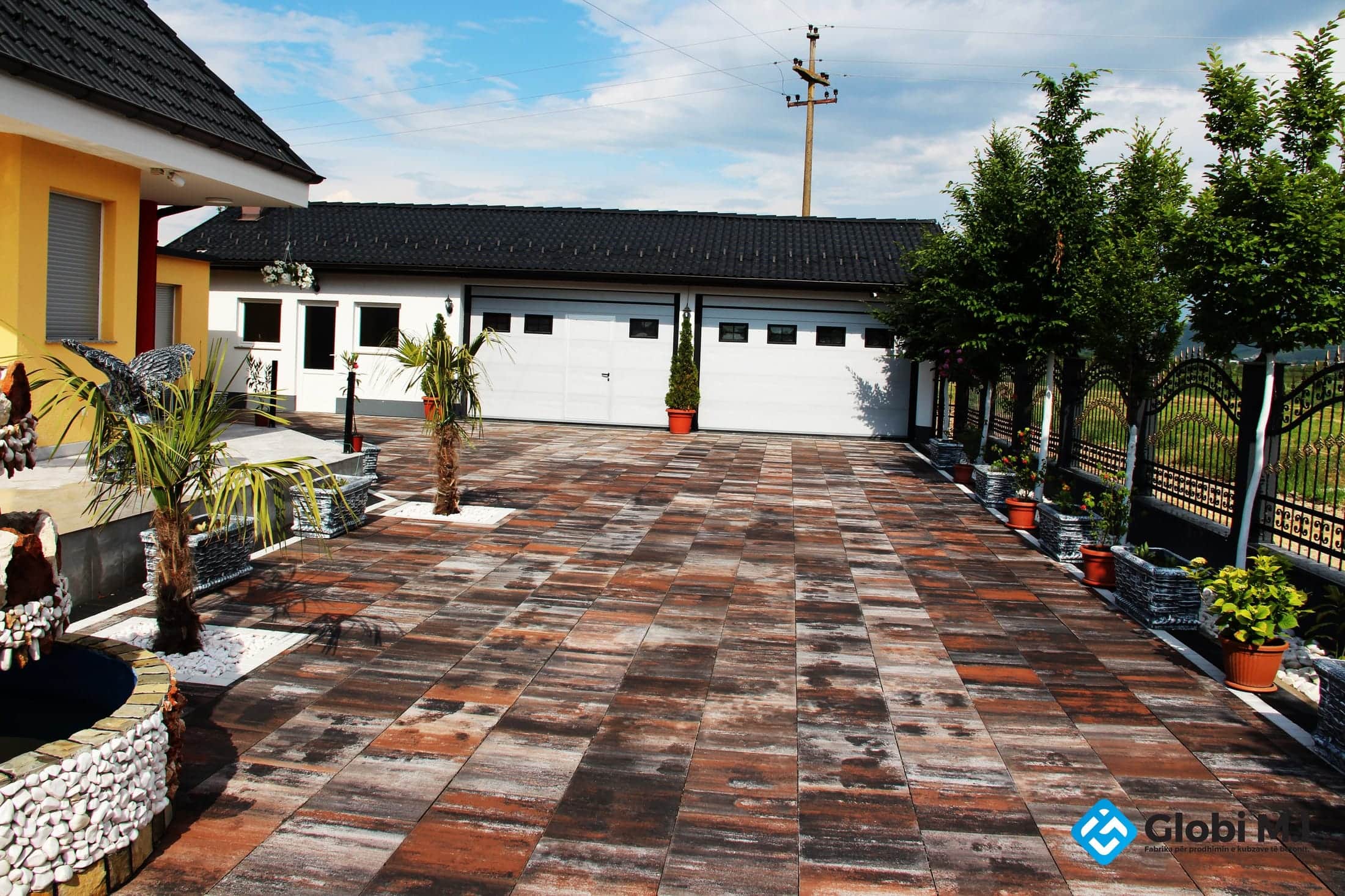 Wide paved courtyard along a long white building with a dark roof, potted plants alongside.