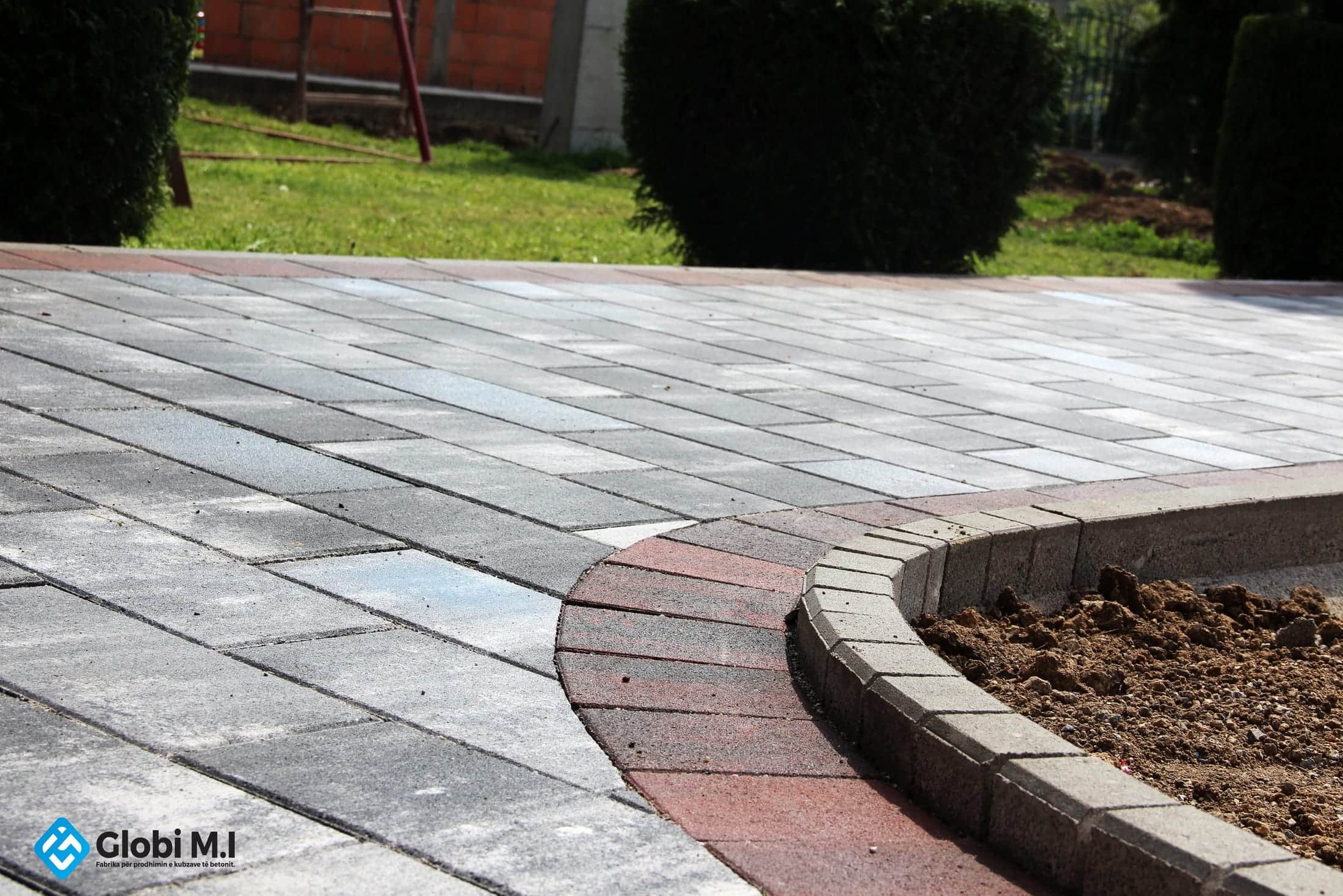 Curved concrete edging closing a bed of soil, beside paving in several colours.