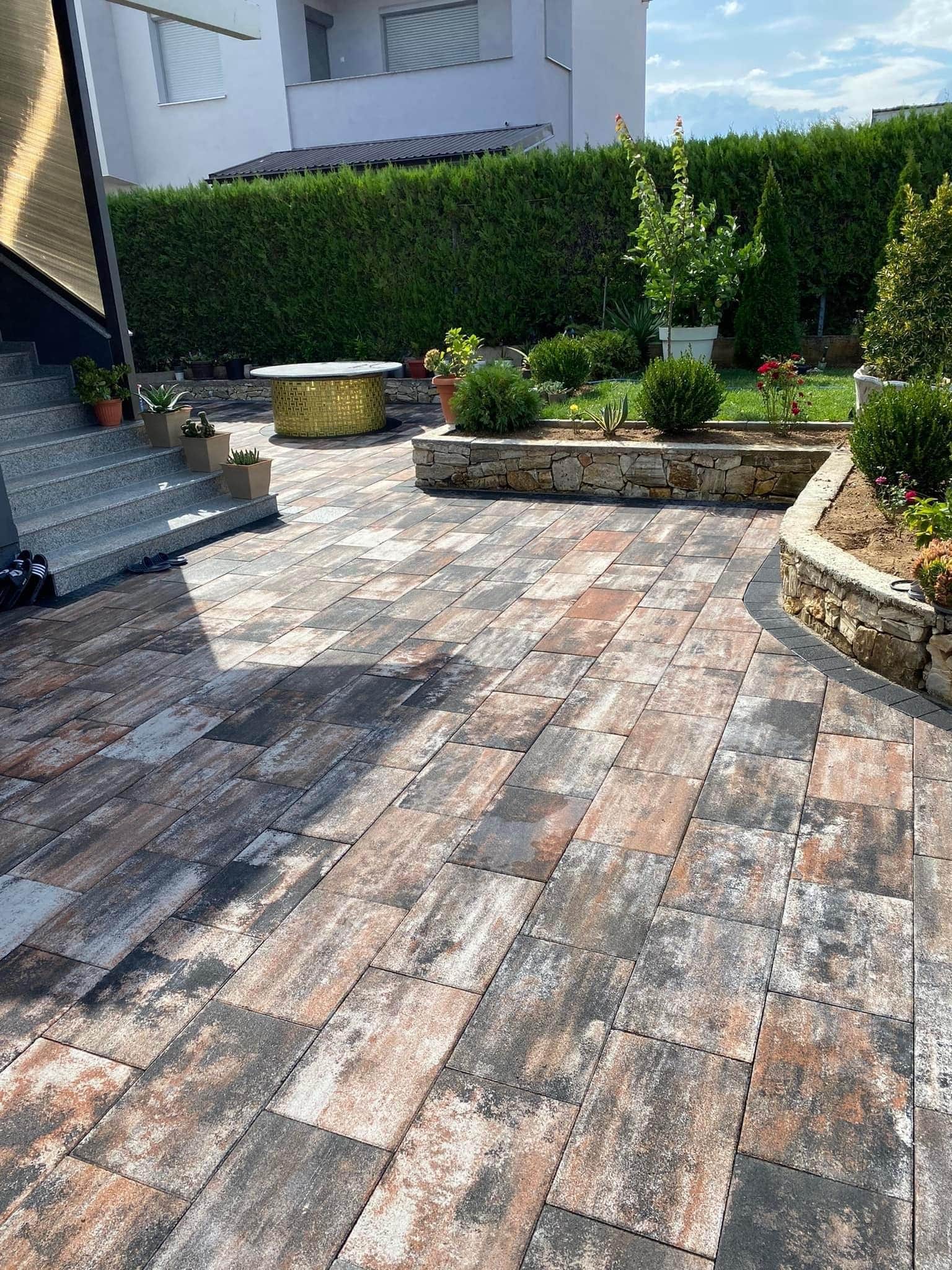 Paved area at the house, with steps rising and a planted bed alongside.