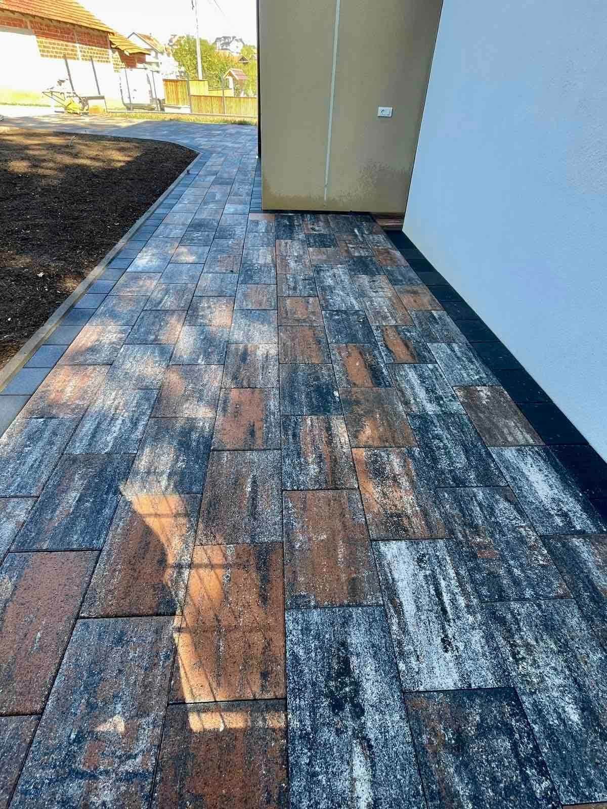 Paved strip turning at the corner of the house, with a bed of dark soil alongside.