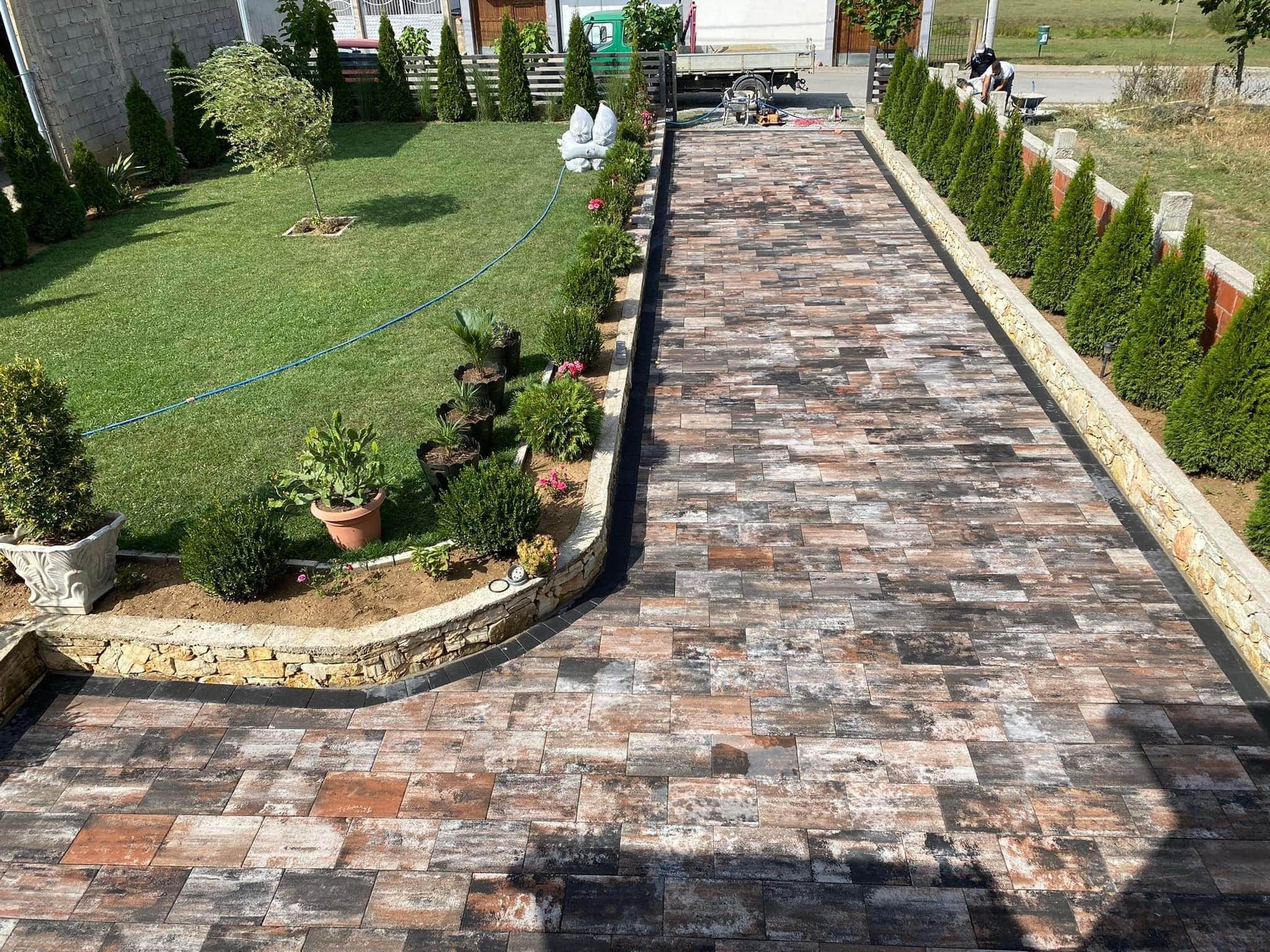 Pflasterfläche in einem Außenbereich mit Begrünung und Betonelementen.