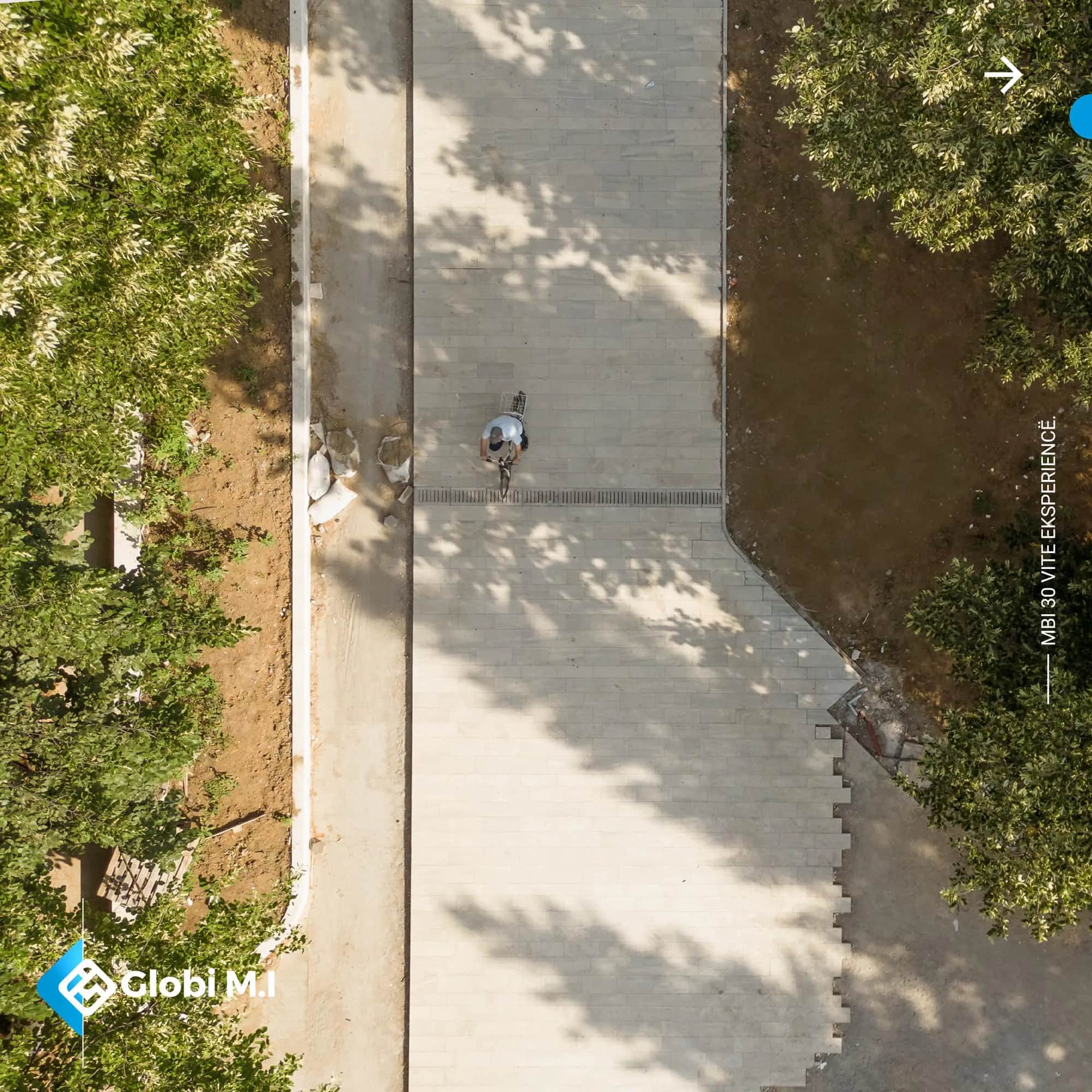 Paved footpath along the boulevard in Kamenicë seen from above, with tree shadows.